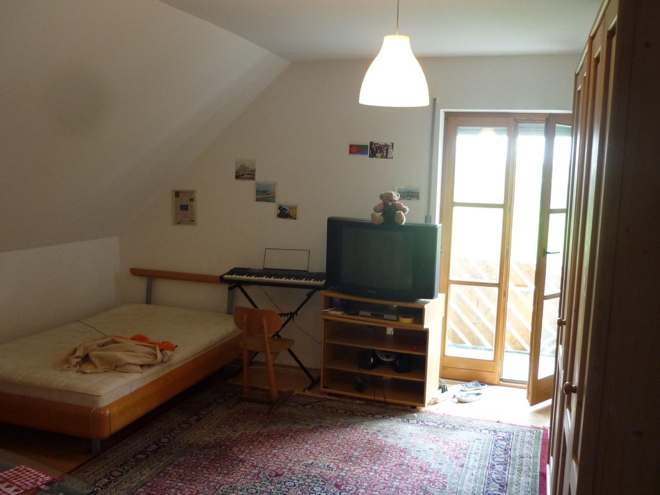 Einzelzimmer unter der Dachschräge mit Bett, Keyboard, Fernseher und Tür auf den Balkon