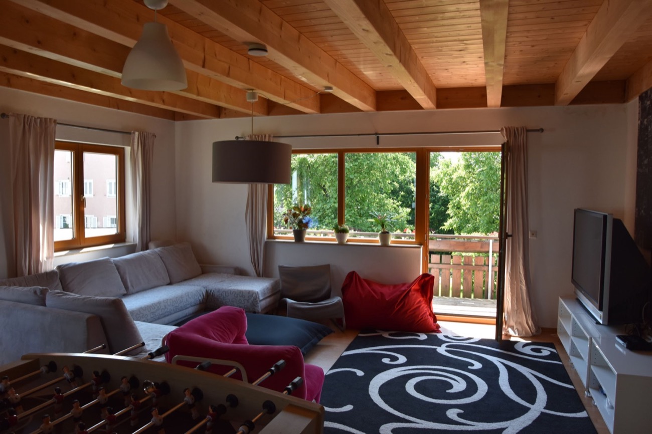 Wohnzimmer der Wohngruppe mit Holzdecke, Sofalandschaft, Sitzsäcken, Kicker und Tür zum Balkon