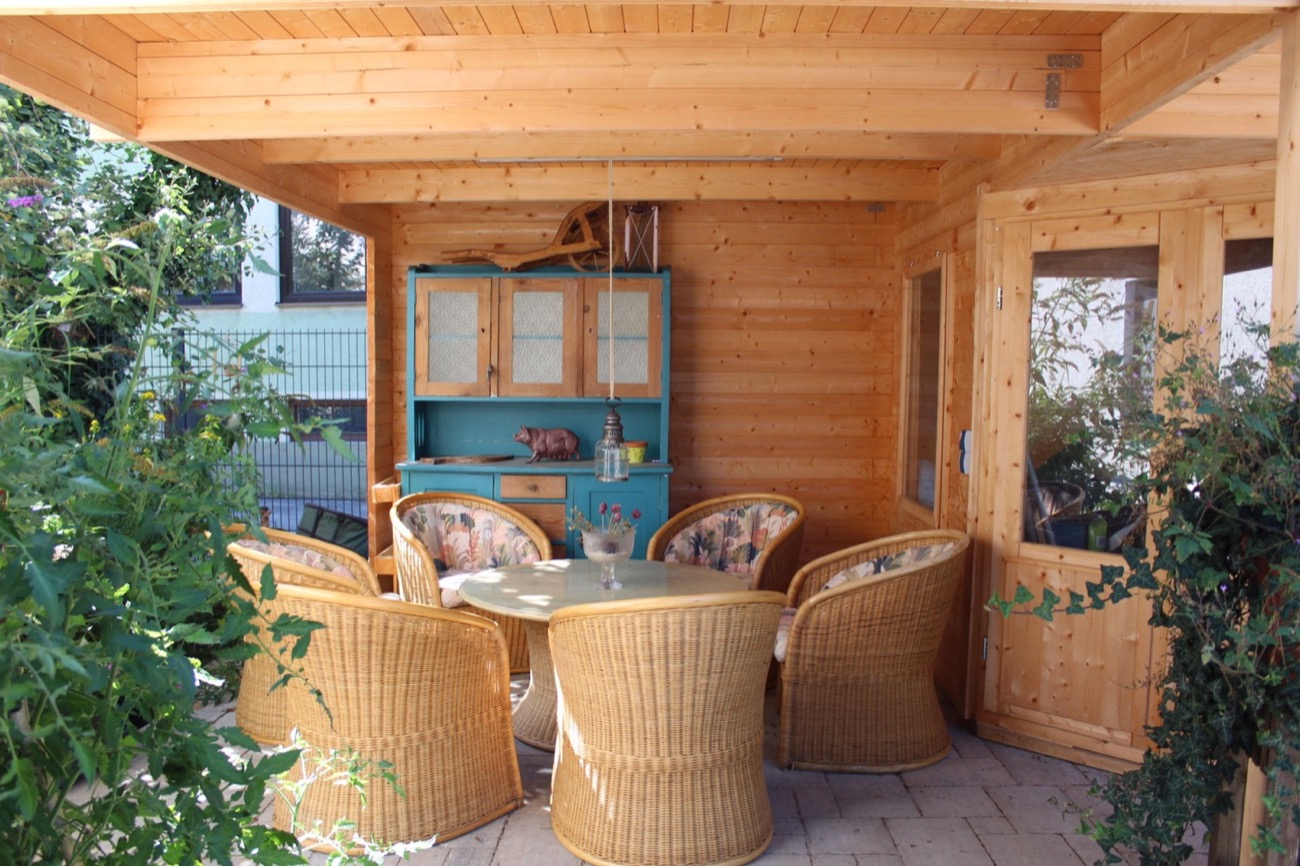 Überdachter Gartenpavillon aus Holz mit Korbstühlen, Tisch und türkisfarbenem Buffetschrank